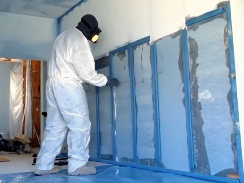 Mold remediation technician in protective gear inspecting water-damaged drywall in a Florida home